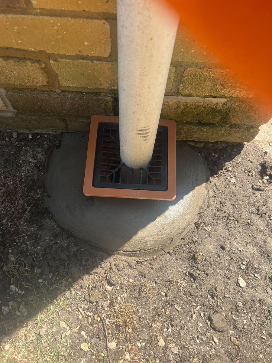 New square gully and grate fitted under a downpipe and haunched in with concrete