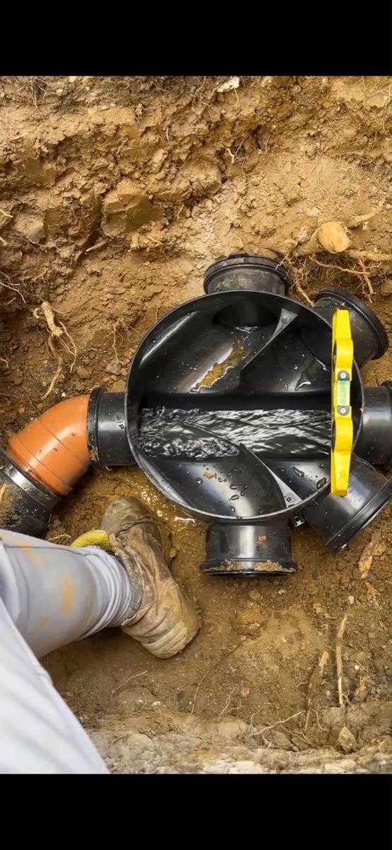 New black plastic inspection chamber set into the ground with a spirit level across it and water running through