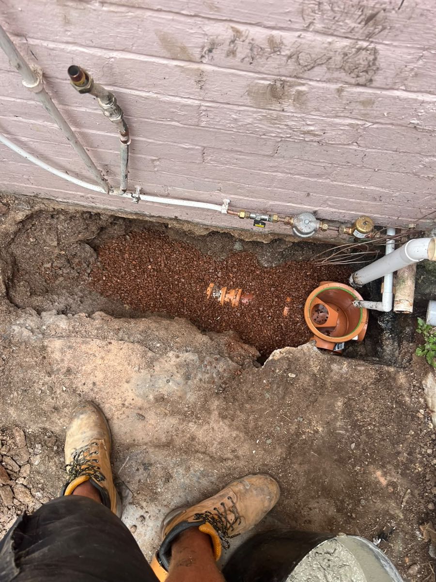 New pipe junction and rodding-eye access bedded in shingle beside a house wall