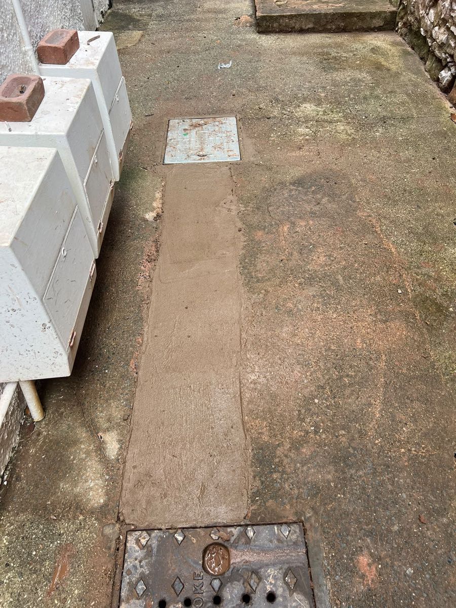 Narrow path with a freshly concreted strip running between two drain covers
